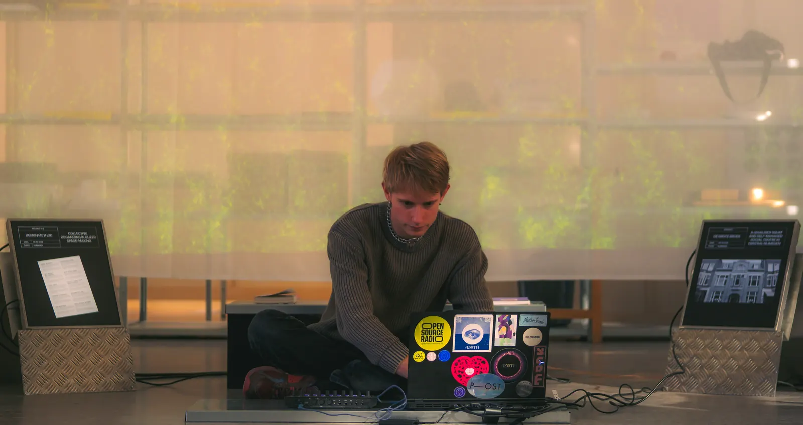 Daan Walder sitting cross legged behind a laptop in front of a softly lit, translucent installation.