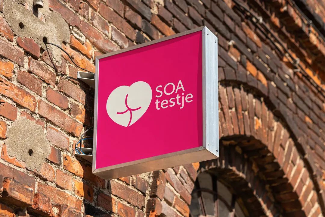 A pink SOA Testje sign on a brick facade